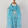 Detailed view of turquoise floral lace scarf with elegant ruffled edges on mannequin - Lake Blue