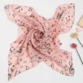 Nahaufnahme eines rosa Seidenschals mit schwarzem Notendruck und weicher Textur. - Rosa Musiknote