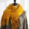 Close-up of mustard yellow thick knit scarf with long tassels draped on a mannequin - 200*70cm / Turmeric
