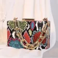 Farbenfrohe Box-Clutch mit Schlangenmuster und einer markanten goldenen Gliederkette - Grün