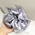 Detailopname van een paarse satijnen scrunchie met elegante zilveren glitter gaasranden - Paars
