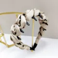 Macro detail view of a champagne satin padded headband with teeth on a gold stand - Light Khaki