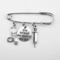 Detailed view of the syringe and stethoscope charms on the silver safety pin brooch - Retro Silver (Inspirational Tag/Stethoscope/Syringe)