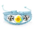Close-up detail of a light blue braided leather bracelet featuring a vibrant sunflower cabochon - 18mm / Light Blue
