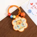 Portachiavi simpatico Capibara con campanellino arancione e charm a fisarmonica. - Capibara che Legge