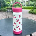 Detailed view of white cherry-print insulated water bottle in outdoor park setting. - 600ml Size / Red (Cherry)