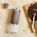 Detail view of the portable manual coffee grinder with wood grain finish and clear container. - Large Head Wood Grain Style