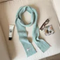 Light blue knit scarf detail showing soft ribbed texture and minimalist brand label design. - Cyan