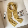 Close-up detail of a cozy yellow ribbed knit scarf styled with aesthetic props on a couch. - Yellow
