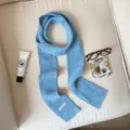 Detail view of a cozy light blue knit scarf with ribbed design and stylish label tag. - Blue