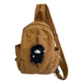 Nahaufnahme der Canvas-Brusttasche mit dem niedlichen schwarzen Schaf-Plüschanhänger. - Braun