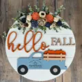 Cartello per porta autunnale in legno rotondo con scritta hello fall, camion blu e decoro floreale. - Targa auto Hello Fall