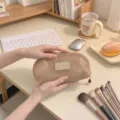Minimalist beige mesh makeup brush bag with shell design held in hands for detail view. - L / Khaki
