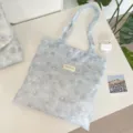 Detailed view of ice blue tie-dye floral tote bag with a woven brand label on white table - Shoulder Bag