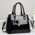 Detail view of a black patent leather handbag with a stylish bow and gold hardware - Black