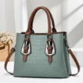 Close-up of sage green embossed crocodile handbag with brown leather handles and buckles. - Green