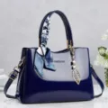 Close-up of a navy blue patent leather handbag with a decorative silk scarf and leaf charm - Blue