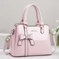 Detailed view of pink patent leather handbag featuring elegant bow and gold logo - Pink