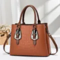 Detail view of the elegant brown crocodile embossed handbag with metal buckle accents. - Earthy Yellow