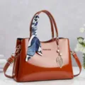 Elegant reddish-brown patent leather handbag with decorative scarf and gold leaf charm - Earthy Yellow