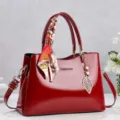 Vista dettagliata di una borsa rossa in vernice con foulard decorativo e ciondolo a foglia. - Rosso