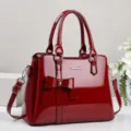 Elegant red patent leather handbag featuring a large stylish bow and glossy finish - Red