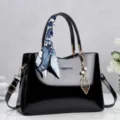 Vista dettagliata di un'elegante borsa a mano in vernice nera con foulard e ciondolo a foglia - Nero