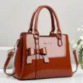 Fashionable glossy brown patent leather handbag featuring a stylish bow and pink panel detail - Earthy Yellow