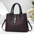 Detail view of stylish dark red textured women handbag with metal lock and top handles. - Coffee