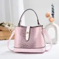 Gros plan sur le sac seau rose gaufré façon crocodile avec son fermoir métallique. - Rose