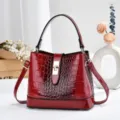 Détail de sac seau rouge vernis gaufré croco, fermeture à serrure élégante et bandoulière. - Rouge