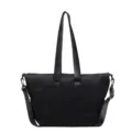 Black canvas tote bag detail view showcasing sturdy shoulder straps and metal hardware components. - Black
