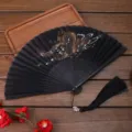 Éventail pliant noir de style traditionnel chinois avec motif dragon doré et gland. - Motif de Dragon Chinois