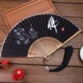 Traditional Chinese folding fan with black fabric, bamboo ribs, and elegant lotus calligraphy design. - 14 Buddha