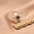 Detailaufnahme von Barockperlen Blumenohrringen mit blauem Mittelstein und Holzmabstab. - Lila (Lila Staubblatt Blume Perle Ohrstecker)