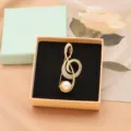 Gold-plated music note brooch with sparkling clear cubic zirconia and elegant white pearl accent. - Music