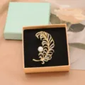 Elegant gold-tone feather brooch with crystal rhinestones and a white pearl accent for women. - Feather