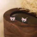 Gros plan de boucles d'oreilles nœud en cristal rose sur un support en bois foncé. - Argent 990 / Style Zircon Rose