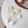 Nahaufnahme von feinen cremefarbenen Baumwollsocken mit süßen Rüschen und grauen Schleifen. - Einheitsgröße / Hellgelb