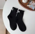 Primo piano di calzini neri al polpaccio con fiocchi bianchi e delicati bordi volant. - Taglia unica / Nero