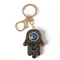 Detailed view of a Hamsa hand keychain featuring a blue evil eye charm and rhinestones. - Black