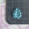 Primer plano detallado de la pequeña hoja tropical de resina en la alfombrilla de corte. - Hoja de Monstera Azul Gris