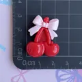 Primo piano di ciondoli in resina di ciliegia rossa e rosa con fiocco per gioielli fai da te. - Fiocco Rosa con Ciliegia Rossa