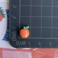 Mini ciondolo frutta in resina vista dettagliata per mostrare le dimensioni su tappetino, accessorio. - Stile Arancia