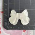 Primo piano di grande fiocco in resina trasparente glitterata, ciondolo per accessori artigianali. - Beige