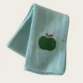 Close up of light blue knitted wool winter scarf featuring a cute green apple pattern detail. - Light Blue