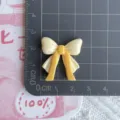 Close-up detail of glossy two-tone resin ribbon bow DIY accessory for phone case and crafts. - Yellow