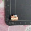 Close-up detail shot of a mini resin bear charm with letters and crown, perfect for DIY crafts. - Coffee