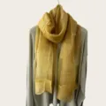 Vista detallada de una bufanda ligera y transparente amarillo mostaza sobre un suéter gris. - 180cm / Amarillo jengibre