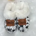 Close-up of customized cow print slippers with white faux fur lining and leather name patches - 36-37 / Cow Print